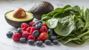 Fresh alkaline ingredients: avocado, spinach, and a variety of berries on a marble countertop