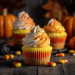 Candy corn cupcakes with tri-color layers and matching frosting on Halloween-themed surface with decorations