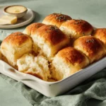 Soft gluten free dinner rolls with golden tops in white baking dish showing pull-apart texture